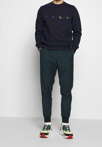 Felpa marina con ricami di cavalli multicolori, abbinata a pantaloni a quadri verdi. Completata con sneakers chunky con accenti neri, bianchi e rossi.