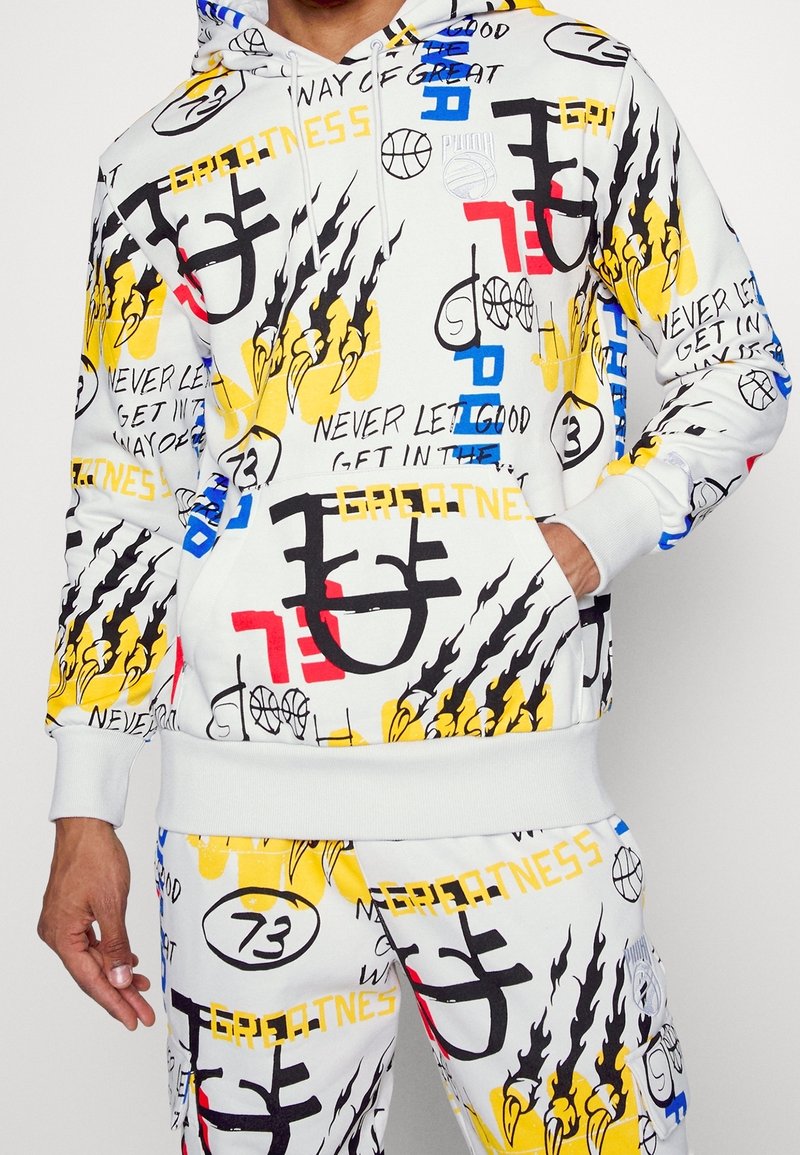 Ensemble sweat à capuche blanc et pantalon avec des imprimés style graffiti en noir, jaune, rouge et bleu incluant des flammes, des ballons de basket et les mots "greatness" et "never let."