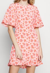 Rosa blommig klänning med korta, svävande ärmar; har en utsvängd fåll och spridda orange och rosa blommönster på ett mjukt tyg.