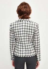 Blazer a cuadros en gris y blanco con bordes deshilachados, corte ajustado y mangas largas. La tela tiene un acabado texturizado. Se muestra la vista posterior.