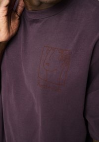 Lilla bomulds T-shirt med rund hals og oversized pasform. Har en minimalistisk stregtegning af et ansigt og ordet "Resteröds" under.