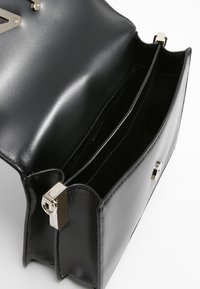 Černá kožená kabelka s hladkou texturou, dvěma vnitřními přihrádkami a zlatými kovovými doplňky ke zavírání, s minimalistickým designem.