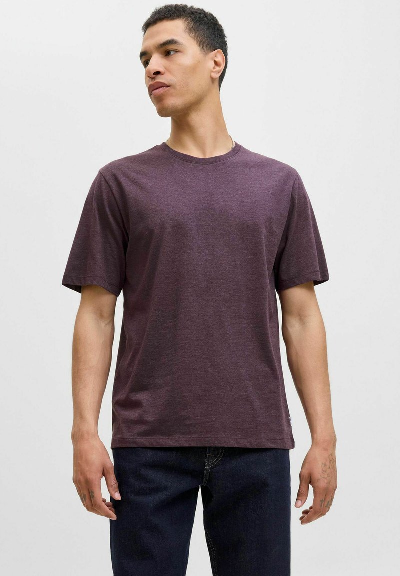 Short-sleeve, crew neck t-shirt in deep purple fabric; relaxed fit with a smooth texture. Paired with dark denim jeans.