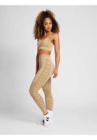 Beige sportbehå och leggings-set med en texturerad design och chevronmönster. Kombinerat med vita sportskor.