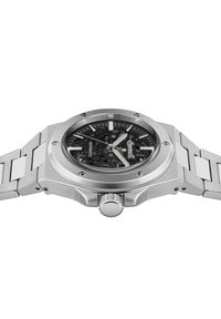 Orologio in acciaio inossidabile argentato con quadrante scheletrato nero, con lancette argento, una corona prominente e un design a bracciale collegato.