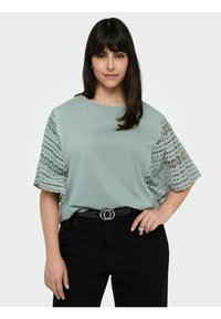 Top azzurro chiaro a maniche corte con dettagli in pizzo decorato sulle maniche, abbinato a pantaloni neri a vita alta e una cintura con fibbia circolare.