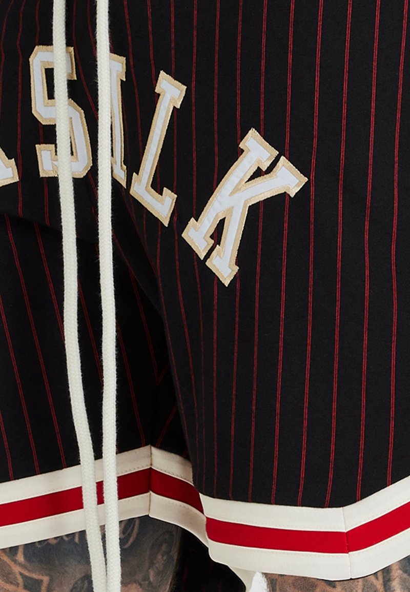 Svarta sportshorts med röda ränder och vit text. Har en vit dragsko och detaljer med röd-vit rand vid fållen.