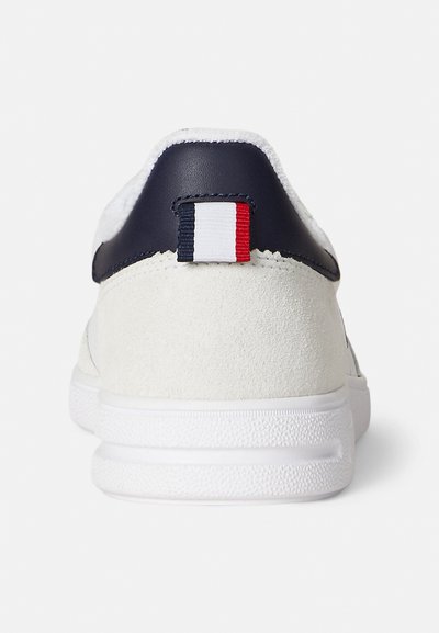 Vita sneakers i mocka med en marinblå läderklack. Har en liten röd, vit och blå flik bak. Texturerad vit gummisula.
