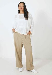 Pull blanc en tricot lâche avec un col rond, associé à un pantalon beige à jambes larges et des baskets blanches. Design texturé, coupe décontractée.