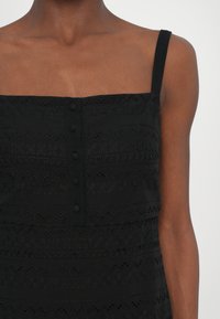 Rochie neagră fără mâneci, cu broderie texturată, decolteu pătrat și închidere cu nasturi pe față. Țesătură netedă, cu un fit structurat.