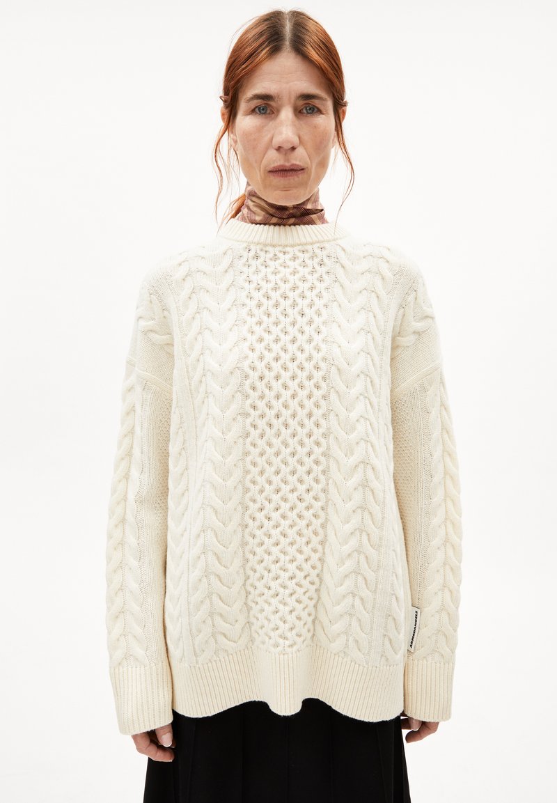 Kabelgebreide trui in crème; heeft textuurpatronen en ribbels aan de mouwen. Losse pasvorm met een ronde zoom en etiket aan de zijnaad.