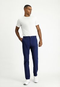Pantalones azul marino fabricados con material ligero, con un corte clásico, frente plano, bolsillos laterales y cierre de botón, combinados con una camiseta blanca.