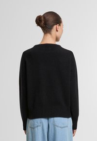 Schwarzer Strickpullover mit Rundhalsausschnitt und geripptem Saum. Weiche Textur, lässiger Schnitt, von hinten mit hellblauen weiten Jeans gezeigt.