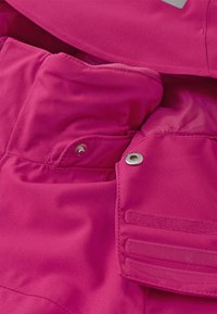 Różowa kurtka izolacyjna o gładkiej fakturze, z zamykanymi na zamek i zatrzaskami kieszeniami, miękką podszewką oraz solidnym detalem szewnym.