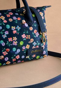 Sac à main en imprimé floral marine en matériau synthétique, arborant des fleurs colorées et des motifs de bonbons, avec des accessoires en or et une étiquette de marque.
