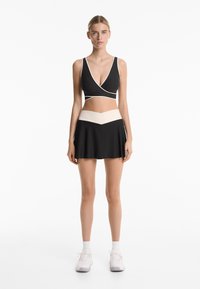 Crni crop top s bijelim obrubom, uparen s crnom suknjom s širom koja ima kontrastnu bež traku u struku i chevron uzorak.