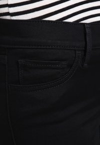 Primer plano de unos pantalones vaqueros negros que presentan un bolsillo frontal y una cinturilla, combinados con una camiseta a rayas en la parte superior. Enfoque en la textura de la tela y las costuras.