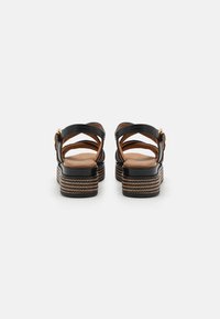 Sandales à plateforme en cuir noir avec des brides croisées, une semelle intérieure beige et un détail de semelle extérieure tressée texturée. Fermeture à boucle réglable au niveau du talon.