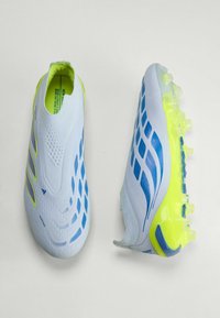Chaussures à crampons blanches et jaune néon avec des accents bleus, une montrant le dessus et l'autre la semelle cloutée, conçues pour un usage sportif.
