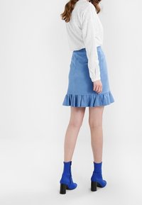 Jupe en jean bleu mini avec ourlet froufroutant, associée à un haut blanc à manches longues et des bottines bleu. Texture lisse et design ajusté.