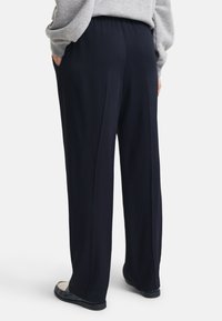 Pantaloni navy a gamba larga con texture liscia, vita elasticizzata e due tasche laterali. Presentano una vestibilità comoda e una leggera drappeggiatura.