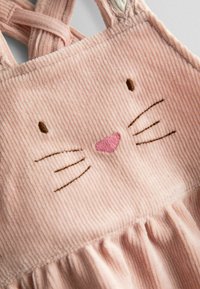 Tela de pana rosa con cara de gato bordada, que incluye ojos marrones, bigotes y una nariz rosa, con detalle fruncido debajo de la cara.