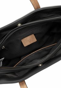 Interno di una borsa a tracolla in pelle nera con una texture liscia, caratterizzato da un'etichetta in pelle beige e una tasca con cerniera in un compartimento spazioso.