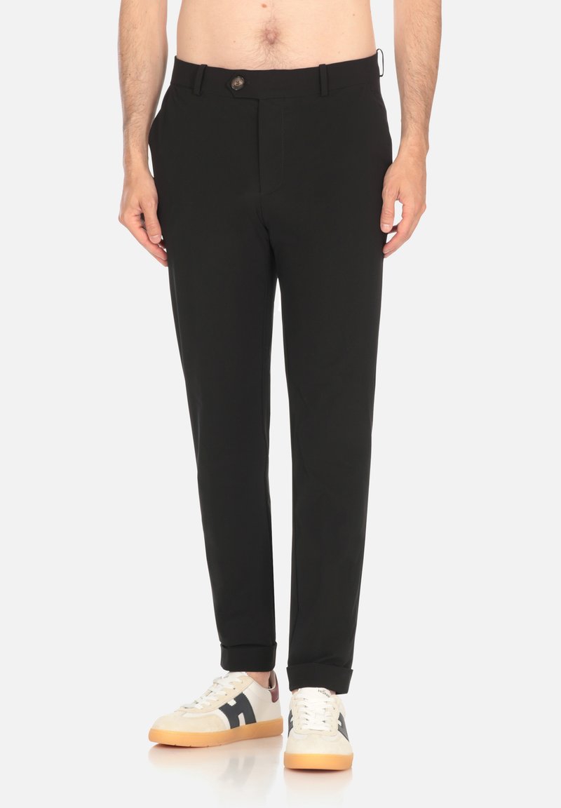 Pantalons légers noirs avec une coupe droite, dotés d'une fermeture à bouton, de passants de ceinture et de poches latérales discrètes. Associés à des baskets blanches.