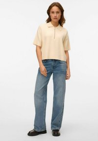 Ljusbeige polo med centralknäppning, korta ärmar, tillsammans med högmidjade blåjeans. Klädseln har en avslappnad passform.