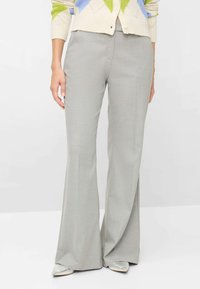 Grå, udvidede bukser med en tekstureret stof, der har en glat talje og diskrete folder ned foran, kombineret med spidse sko.