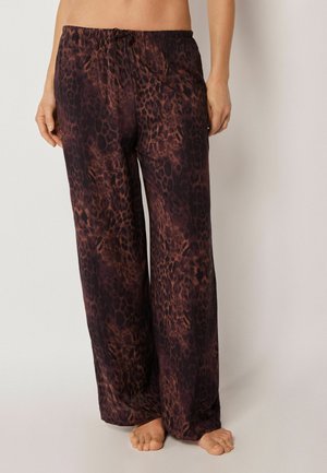 Locker sitzende braune und schwarze Leopardenmuster-Hose, barfuß getragen von einer Person vor einem schlichten Hintergrund.