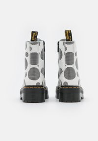 Witte enkellaarzen met zwarte stippen en gestreepte patronen, met een stevige zwarte zool en een gele lus, gladde textuur en decoratieve stiksels.