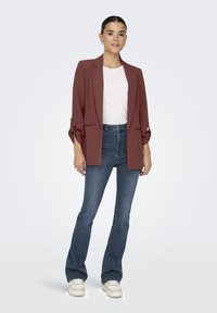 Bordeauxblazer met een ontspannen pasvorm, witte textuur top, hoge blauwe flared jeans en crèmekleurige sneakers. Eenvoudige oorbellen als accessoires.