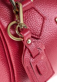 Borsa a tracolla in pelle rossa testurizzata con hardware dorato. Presenta una chiusura con zip, una tracolla staccabile e un piccolo tag con attacco a loop.