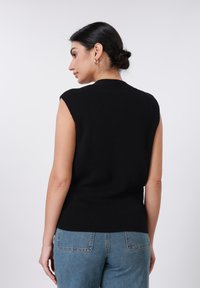 Μαύρο αμάνικο τοπ με υφή ριμπ, ψηλό λαιμόκοψη και εφαρμοστή μέση; σε συνδυασμό με ανοιχτόχρωμο τζιν παντελόνι. Απλός σχεδιασμός.