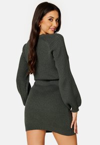 Abito a maglia rigata verde scuro con maniche lunghe a sbuffo e vita aderente, caratterizzato da un orlo che arriva a metà coscia e un tessuto testurizzato.