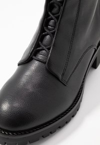Černé kožené kotníkové boty s texturovaným povrchem, šněrováním v přední části a pevnou podrážkou s drsným vzorem pro lepší přilnavost.