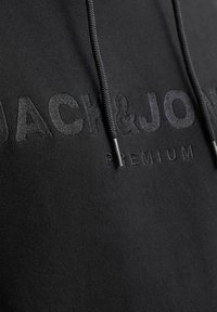 Felpa nera con logo ricamato che presenta "JACK & JONES" e "PREMIUM" in basso. Include coulisse con punte metalliche. Texture morbida.