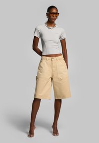 T-shirt aderente grigio chiaro a maniche corte, abbinato a pantaloni cargo beige al ginocchio con tasche e una leggera texture in denim.