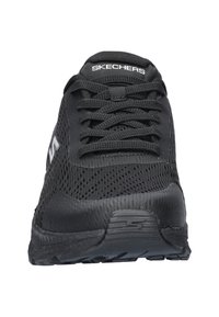 Zapatilla deportiva negra con parte superior de malla texturizada y cordones, con un logotipo en el costado y una suela de goma resistente para un buen agarre.