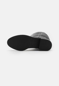 Botas de tobillo negras con una suela de goma texturizada y un empeine suave y brillante. Presenta detalles cosidos a lo largo de los lados. Talla 39.