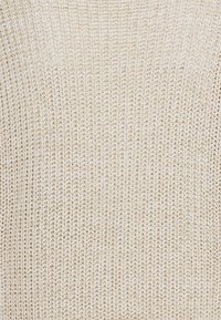 Světlý béžový pletený svetr s texturovaným vzorem a volným tkaním. Materiál vypadá měkce a útulně, vhodný pro vrstvení nebo neformální nošení.