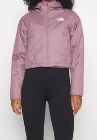 Kort, lätt jacka i ljuslila, tillverkad av vattentåligt material. Har en framtida dragkedja, huva och en diskret logga på bröstet.