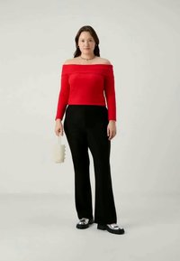 Red ribbed off-shoulder top paired with black flared pants. Accessories include a white textured handbag and black lace-up shoes with silver accents.