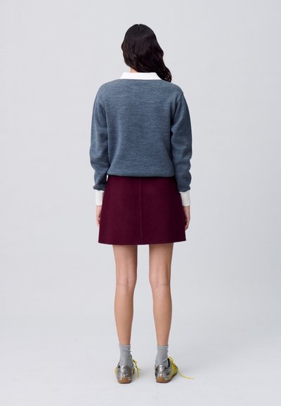 Suéter de punto gris con cuello blanco, combinado con una falda burdeos. Zapatos plateados con cordones amarillos, calcetines grises. Diseño simple y estructurado.