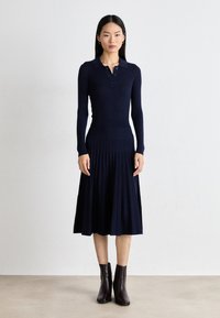 Navy ribbed knit dress with a polo collar, long sleeves, and pleated skirt. Paired with chocolate brown ankle boots.