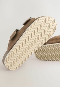 Bruna mocka skor med två justerbara remmar, med en strukturerad beige gummisula med ett vågigt mönster och grå accenter.