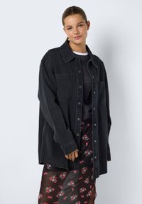 Svart denim oversized skjorta med krage, framknäppning och två bröstfickor, matchad med en blommig transparent kjol.