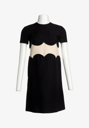 Robe noire à manches courtes avec une découpe beige festonnée autour de la taille, présentée sur un buste de mannequin blanc.