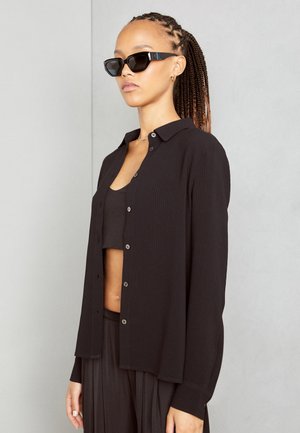 Black ribbed blouse with a collar, front buttons, and long sleeves. Worn over a matching black sleeveless top. For modern layering.